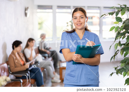 Young female therapist standing with papers in lobby of clinic 102392328