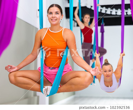 Girl sitting in butterfly pose in suspended hammock with fingers folded in mudra Girl sitting in butterfly pose in suspended hammock with fingers folded in mudra 102392536