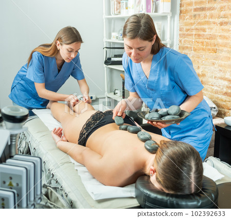 Two masseuses massage the legs and perform a stone therapy procedure Two masseuses massage the legs and perform a stone therapy procedure 102392633
