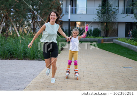 Mother helps daughter learn to roller skate.  102393291