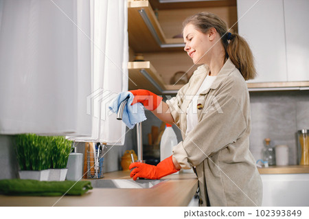Portrait of a woman cleaning in a kitchen and wearing red gloves. Caucasian woman doing housework. Woman holding a rug and wiping a tape. Portrait of a woman cleaning in a kitchen and wearing red gloves. Caucasian woman doing housework. Woman holding a rug and wiping a tape. 102393849