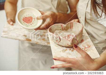 Mutual creative work. Young beautiful couple in casual clothes and aprons. People holds ceramic dishes. 102393863