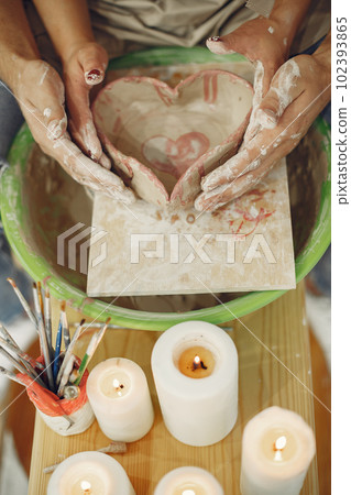 Mutual creative work. Young beautiful couple in casual clothes and aprons. People creating a bowl on a pottery wheel in a clay studio. Mutual creative work. Young beautiful couple in casual clothes and aprons. People creating a bowl on a pottery wheel in a clay studio. 102393865