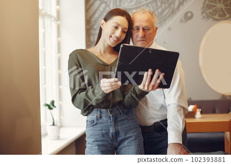 Grandfather with granddaughter. Girl teaching her grandfather. Using a tablet. Grandfather with granddaughter. Girl teaching her grandfather. Using a tablet. 102393881
