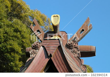 Old faded goldwork corner ridge ornament and tiled roof of a shrine against a blue sky. 102394314