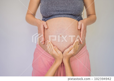 Young beautiful pregnant woman and eldest son. The cute boy put his hands on his mother's belly. Expecting a baby in the family concept. Preparing an older child for a younger one Young beautiful pregnant woman and eldest son. The cute boy put his hands on his mother's belly. Expecting a baby in the family concept. Preparing an older child for a younger one 102394942