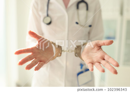 Doctor with stethoscope in handcuffs. Nurse with metal handcuffs on hands Doctor with stethoscope in handcuffs. Nurse with metal handcuffs on hands 102396343