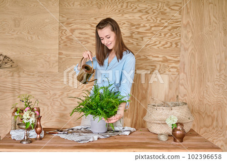 Woman watering a fern, a houseplant. Concept of home garden. Flower and garden shop. 102396658