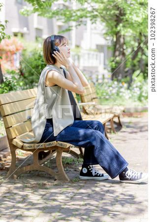 Young woman listening to music with headphones in the fresh green 102398267