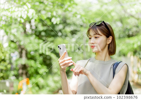 A female college student using a smartphone in the fresh green A female college student using a smartphone in the fresh green 102398676