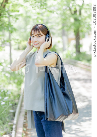Young woman listening to music with headphones in the fresh green 102398898