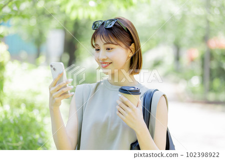 A female college student using a smartphone in the fresh green A female college student using a smartphone in the fresh green 102398922