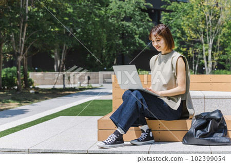 Female college student using a laptop outdoors Female college student using a laptop outdoors 102399054