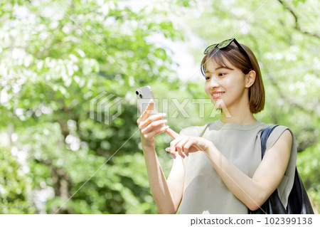 A female college student using a smartphone in the fresh green A female college student using a smartphone in the fresh green 102399138