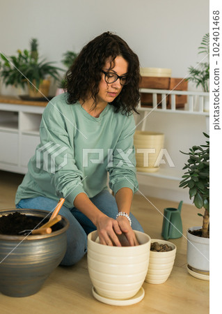Smiling young woman and pot with plant happy work in indoor garden or cozy home office with different houseplants. Happy millennial female gardener or florist take care of domestic flower Smiling young woman and pot with plant happy work in indoor garden or cozy home office with different houseplants. Happy millennial female gardener or florist take care of domestic flower 102401468