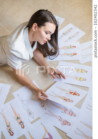 A woman lies on the floor and looks at sketches of swimwear and underwear. A woman lies on the floor and looks at sketches of swimwear and underwear. 102402342