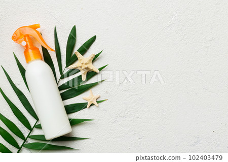 Sunscreen spray bottle. Bottle with sun protection cream and sea shells with tropical green leaf on color background, top view 102403479