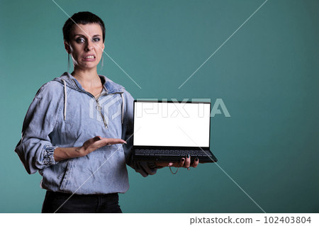 Disappointment unhappy woman presenting laptop computer with blank screen for copyspace in studio with isolated background. Sad angry female doing dislike gesture and expression 102403804