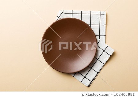 Top view on colored background empty round brown plate on tablecloth for food. Empty dish on napkin with space for your design Top view on colored background empty round brown plate on tablecloth for food. Empty dish on napkin with space for your design 102403991