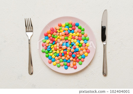 cutlery on table and sweet plate of candy. Health and obesity concept, top view on colored background cutlery on table and sweet plate of candy. Health and obesity concept, top view on colored background 102404001