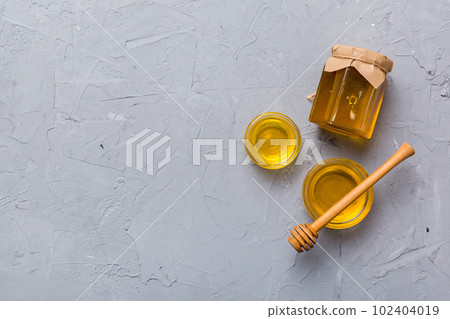 Glass jar of honey with wooden drizzler on colored background. Honey pot and dipper high above. Top view copy space 102404019