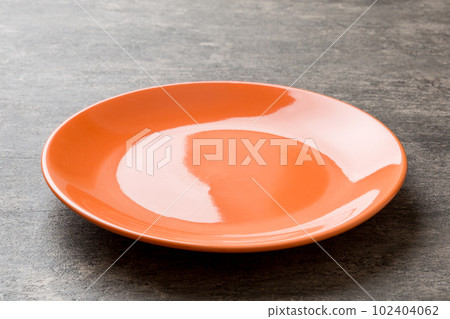 Perspective view of empty orange plate on cement background. Empty space for your design 102404062