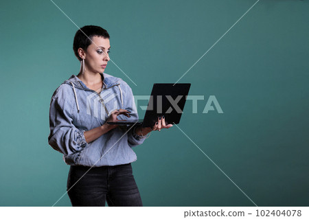 Confident woman holding laptop computer typing business strategy working at financial project in studio with isolated background. Positive female collaborating with remote colleagues Confident woman holding laptop computer typing business strategy working at financial project in studio with isolated background. Positive female collaborating with remote colleagues 102404078