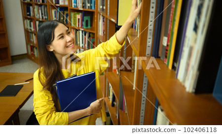 Cheerful Asian female student taking book from shelf in library. Education, knowledge and people concept Cheerful Asian female student taking book from shelf in library. Education, knowledge and people concept 102406118