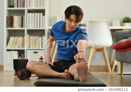 Full length of young fitness man stretching his legs while warming up before morning workout at home Full length of young fitness man stretching his legs while warming up before morning workout at home 102406212