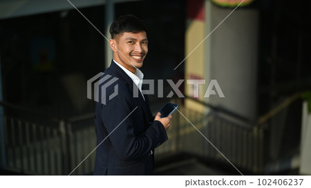 Portrait of smiling young entrepreneur in black suit walking down stairs in office building Portrait of smiling young entrepreneur in black suit walking down stairs in office building 102406237