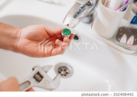 A plumber cleans a water purification filter in faucet faucets in a washbasin 102406442