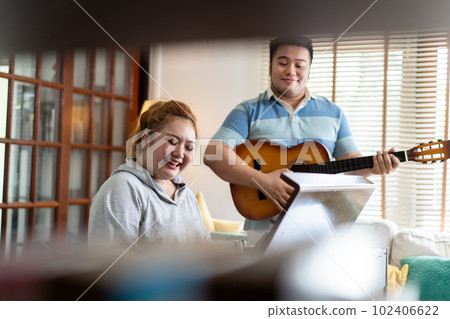Young Asian chubby couple singing and playing acoustic guitar and piano together. Man and woman enjoying musical instrument. People in a band practicing in the house 102406622