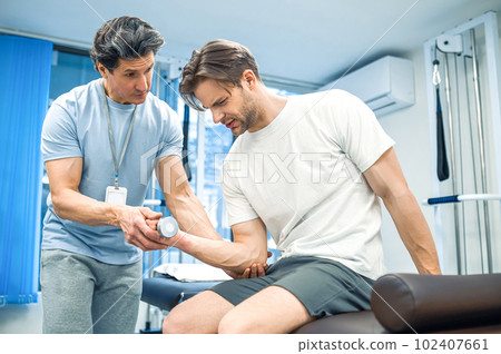 Male patient sitting on a couch and exercising his arm Male patient sitting on a couch and exercising his arm 102407661