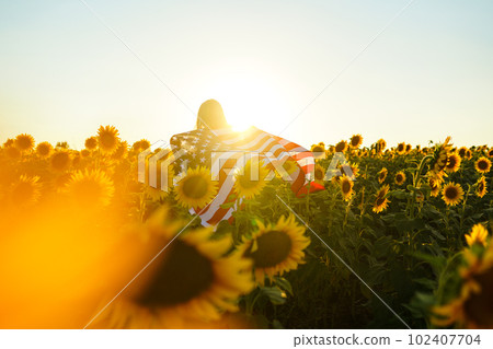 Beautiful girl with the American flag in a sunflower field. 4th of July. Fourth of July. Freedom. 102407704