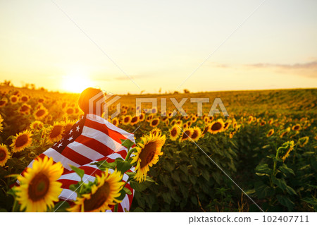 Beautiful girl with the American flag in a sunflower field. 4th of July. Fourth of July. Freedom. 102407711
