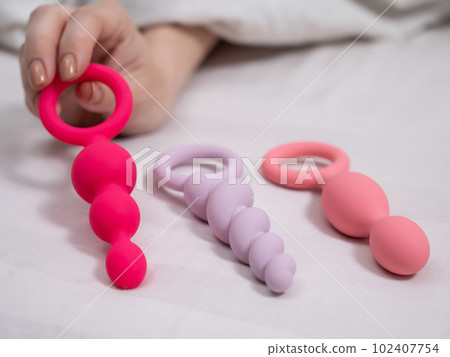 A woman chooses anal beads from a set while lying in bed. A woman chooses anal beads from a set while lying in bed. 102407754