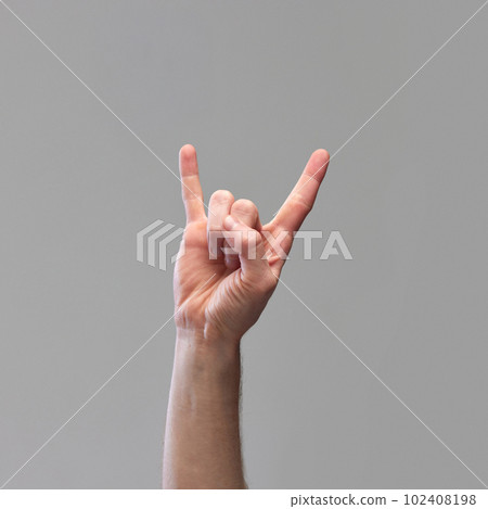 Male hand showing gesture of rock and roll, Hook 'Em Horns against grey background. Having good time signal 102408198