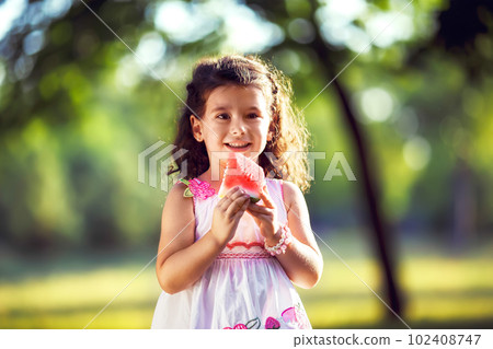 Funny kid eating watermelon outdoors in summer park, focus on eyes. Child, healthy food. Youth lifestyle. Funny kid eating watermelon outdoors in summer park, focus on eyes. Child, healthy food. Youth lifestyle. 102408747