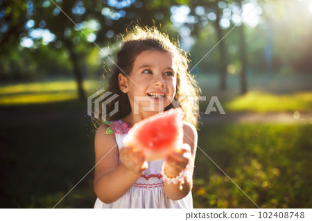 Funny kid eating watermelon outdoors in summer park, focus on eyes. Child, healthy food. Youth lifestyle. 102408748