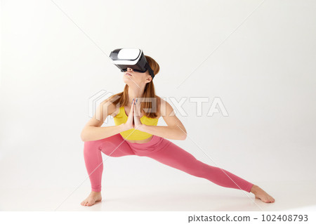 Portrait with young girl wearing sportswear and VR glasses doing yoga exercise over white background. Virtual sport training Portrait with young girl wearing sportswear and VR glasses doing yoga exercise over white background. Virtual sport training 102408793