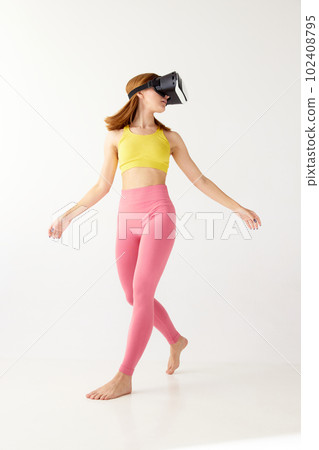 Portrait with young girl in sportswear and VR headset glasses in motion over white background. Youth and virtual lifestyle of future. Time to play 102408795
