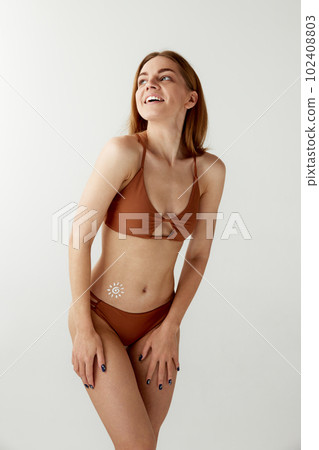 Portrait with young, smiling girl, woman in swimsuit using sunscreen cosmetic, spf on belly over white color studio background 102408803