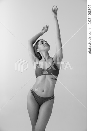 Portrait with young, smiling girl, woman in swimsuit using sunscreen cosmetic on body over white color studio background. Monochrome 102408805