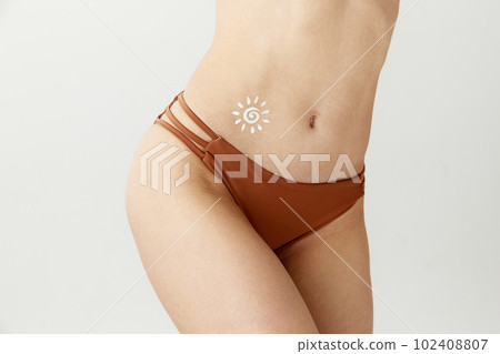 Cropped image of slim female body with light skin in swimsuit with sunscreen on belly over white color studio background. Sun protection lotion, cream Cropped image of slim female body with light skin in swimsuit with sunscreen on belly over white color studio background. Sun protection lotion, cream 102408807