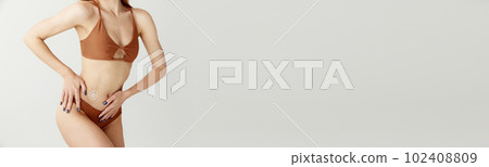Cropped image of slim female body with light skin in swimsuit with sunscreen on belly over white studio background. Banner with copy space for ad 102408809