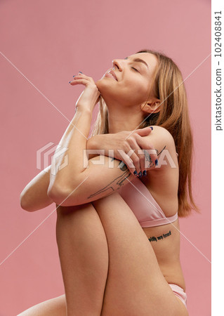 Portrait of happy smiling girl, model wearing swimsuit looking up with closed eyes and dreaming over pink studio background 102408841