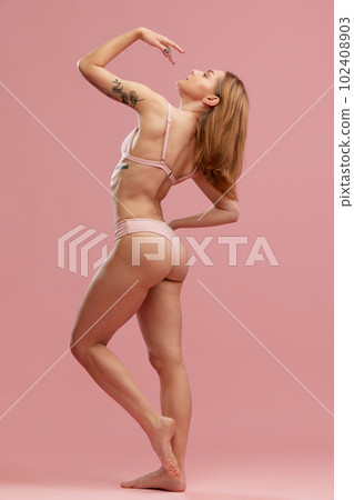Side portrait with sensual slender girl with soft hair wearing beige underwear posing over pink background. Female fitness program 102408903