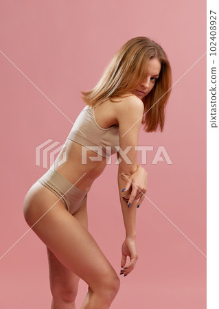 Charming girl, fashion model with soft hair wearing beige underwear posing over pink background. Anti-cellulite program Charming girl, fashion model with soft hair wearing beige underwear posing over pink background. Anti-cellulite program 102408927