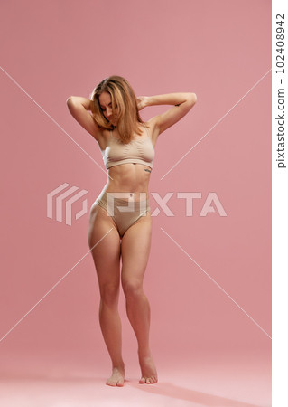 Shot with young girl, model wearing beige underwear posing and looking down over pink studio background. Natural beauty Shot with young girl, model wearing beige underwear posing and looking down over pink studio background. Natural beauty 102408942
