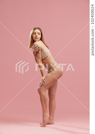 Beautiful slender girl, fashion model with silk hair wearing beige underwear posing over pink background. Body and skin care 102409024